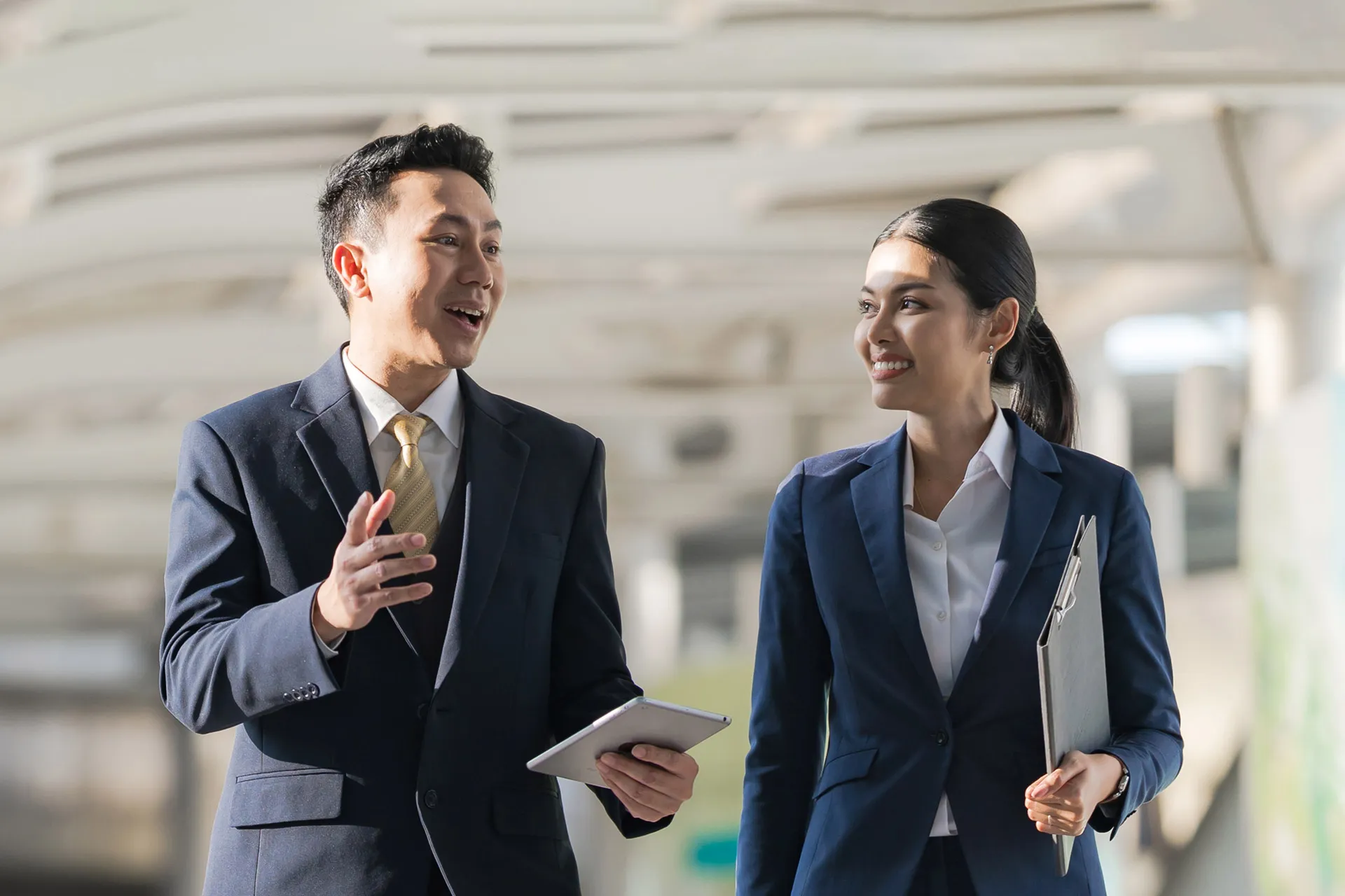 Asian business professionals talking and smiling while walking outdoors.