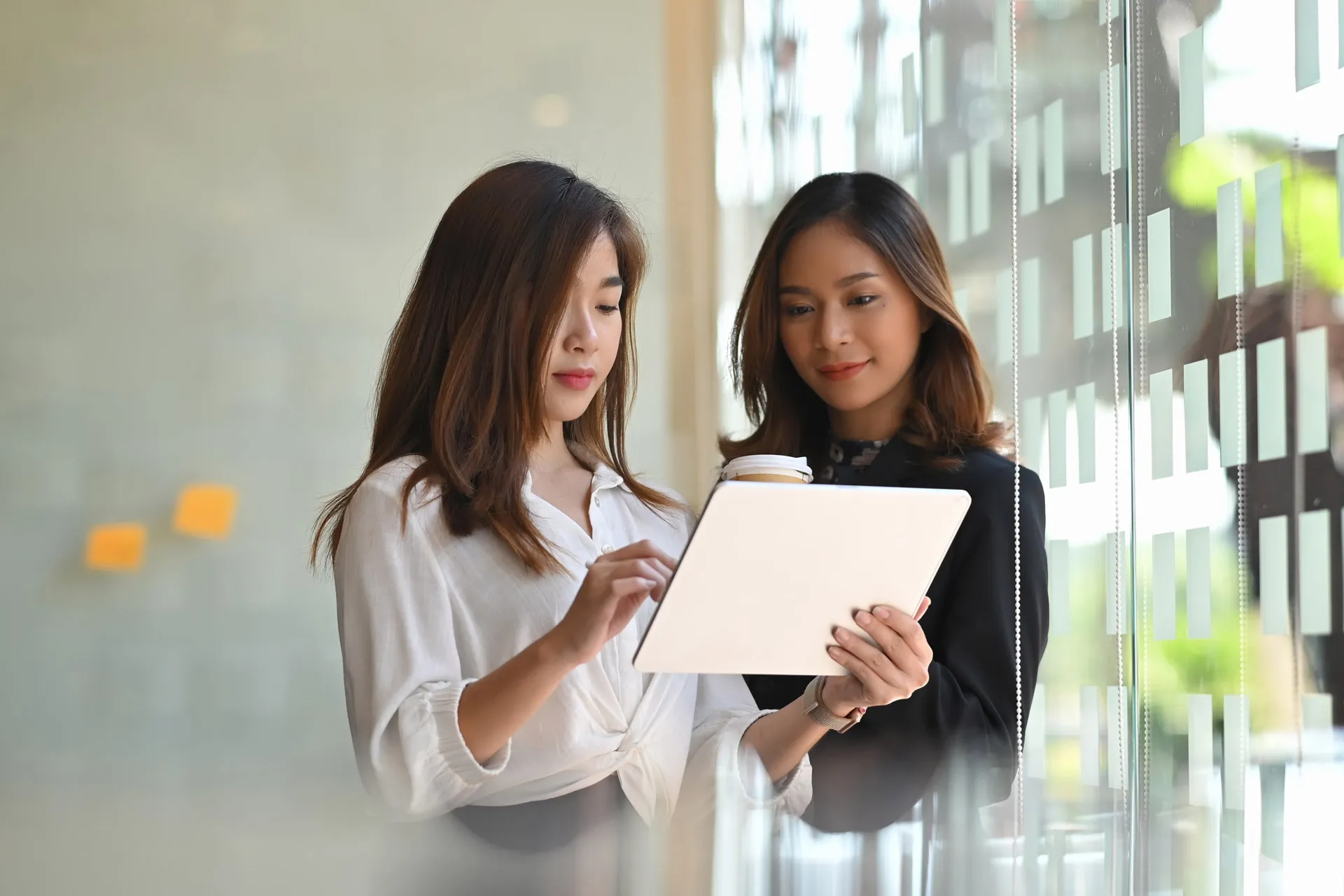 Two Asian women focused on a tablet screen, engrossed in the content displayed.