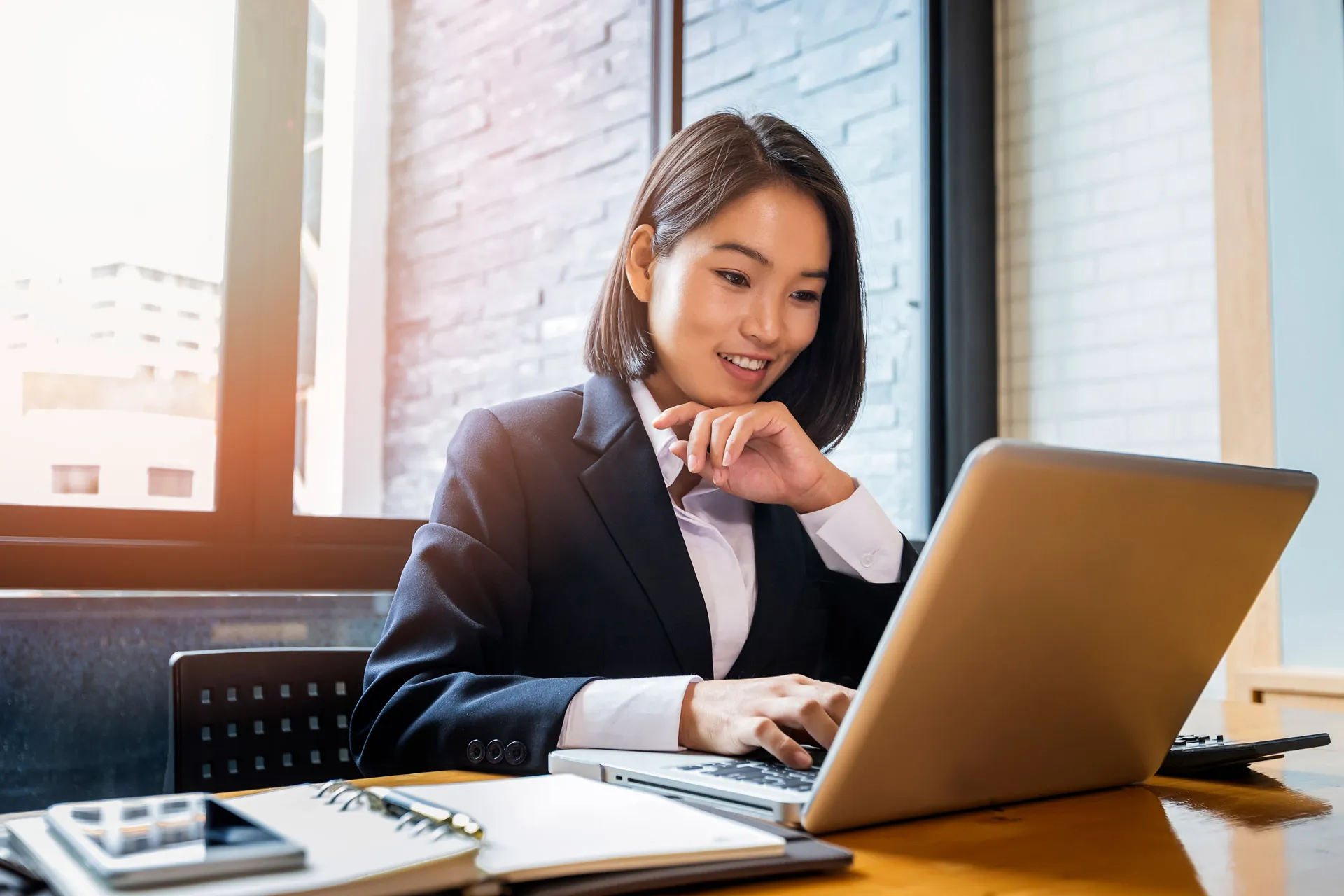 An Asian businesswoman focused on her laptop, diligently working in her office.