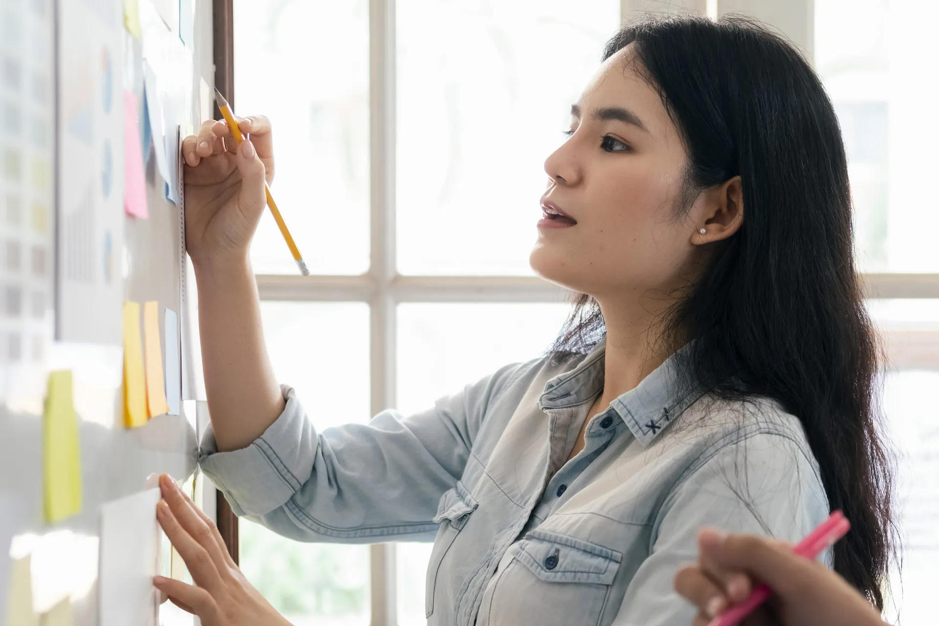 An Asian woman actively engages in a collaborative session, writing on a whiteboard alongside other individuals.