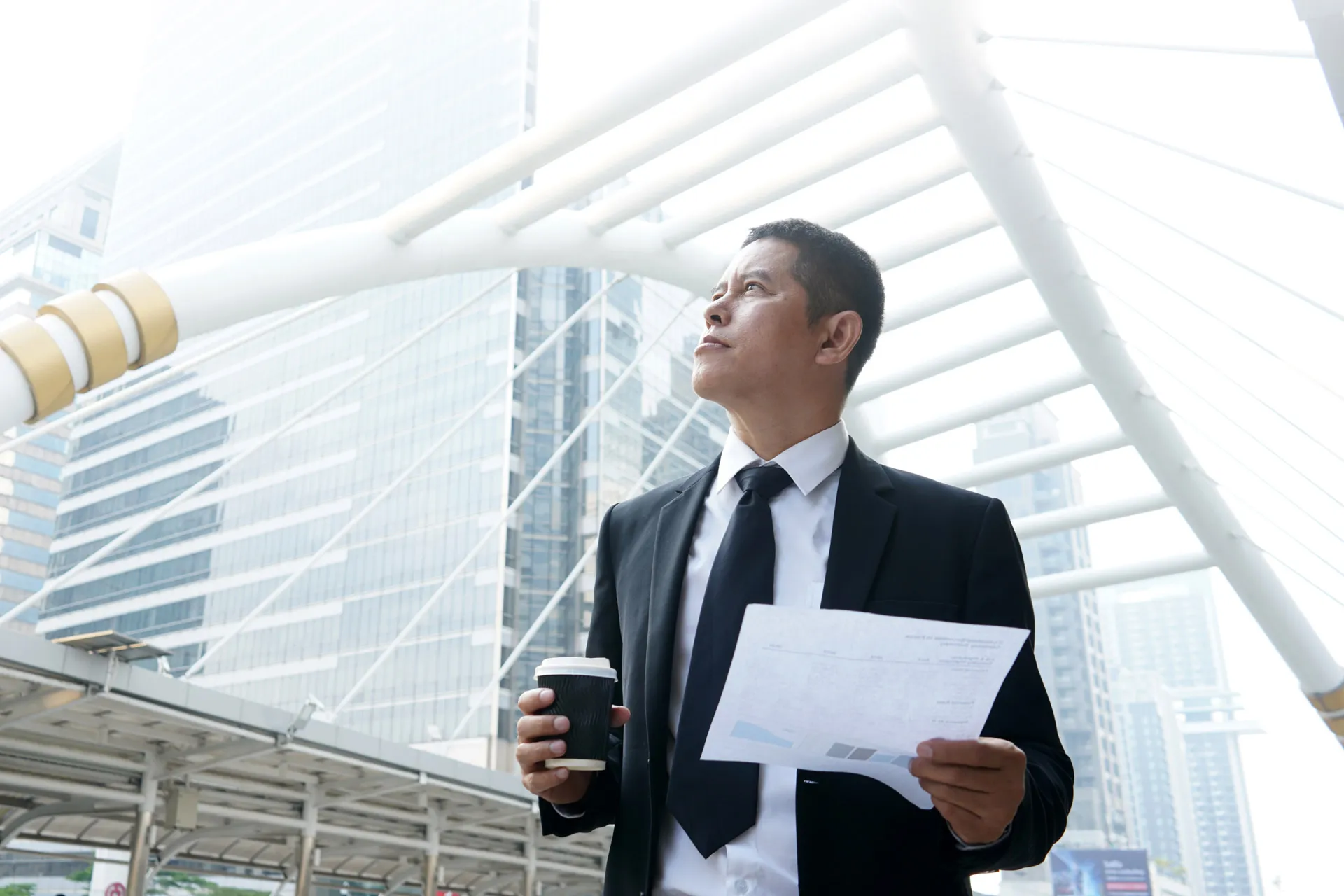 A professional man in a suit and tie walking with a paper and a cup of coffee in hand.