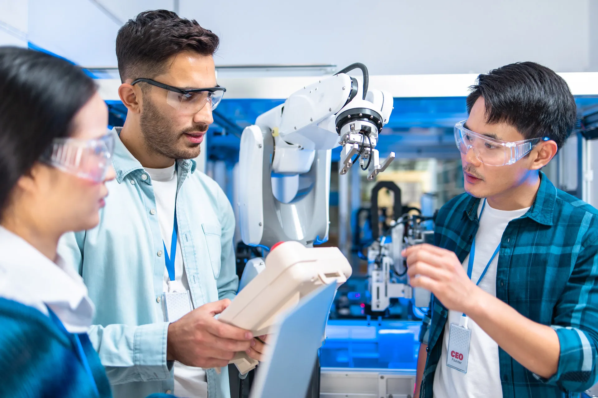 Two men and a woman working with a robotic arm in an industrial setting.