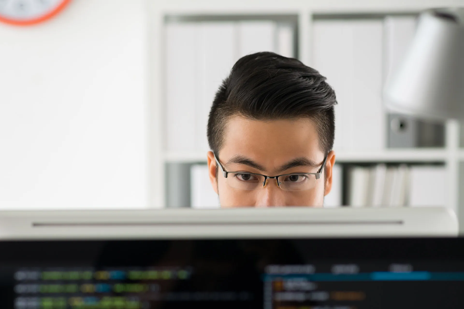 A man wearing glasses intently gazes at a computer screen, focusing on the information displayed.